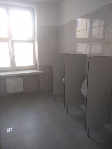 widok sanitaritau kabiny w wc męskim kafelki na podłodze i scianach, okno, kaloryfer