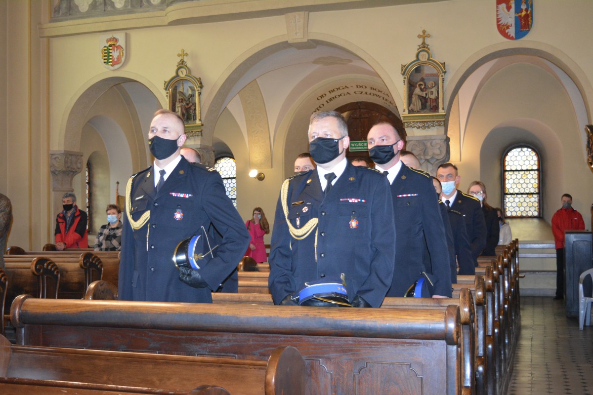 Mężczyźni  w mundurach strażackich stoją w ławach kościelnych
