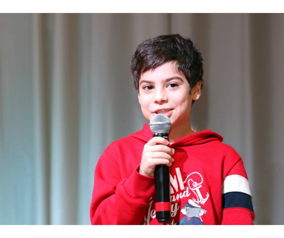 Chłopiec w czerwonej bluzie trzyma w ręku mikrofon