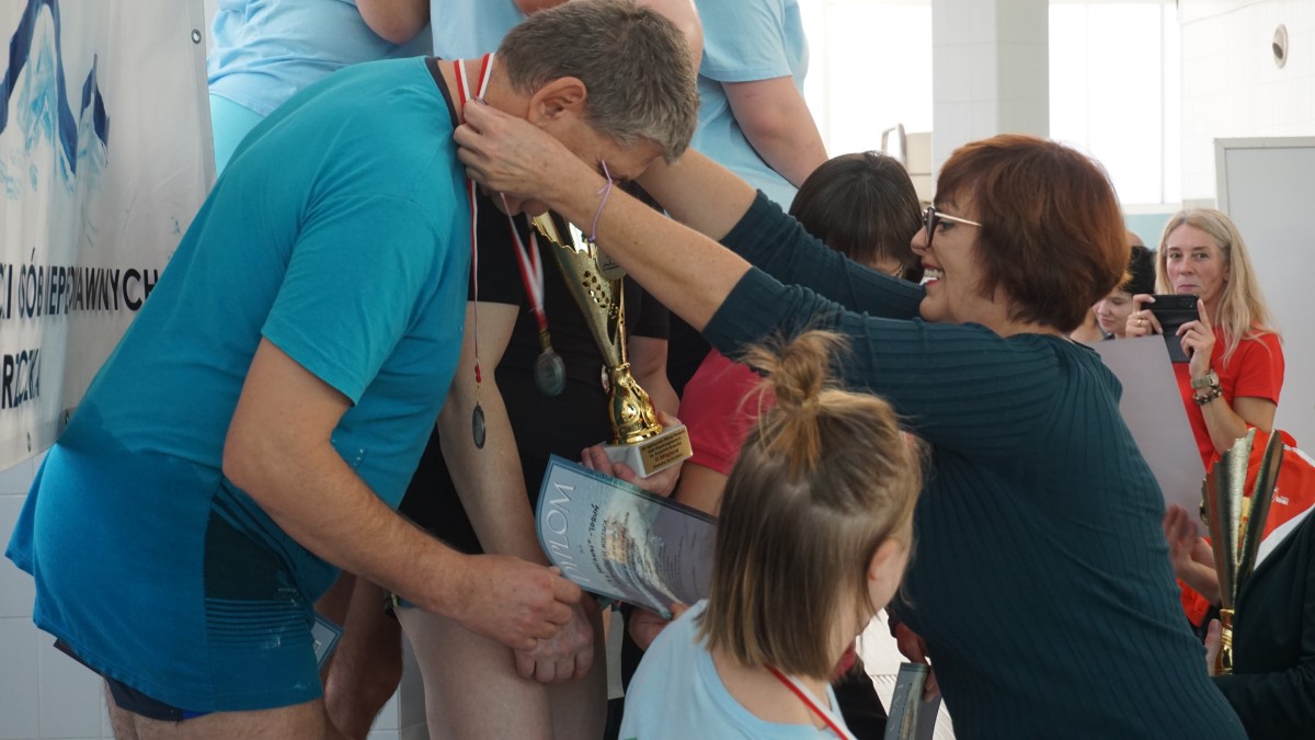 Wicestarosta Ewa Jędrysik zawiesza na szyi jednego z uczestników medal. W tle inni uczestnicy zawodów.