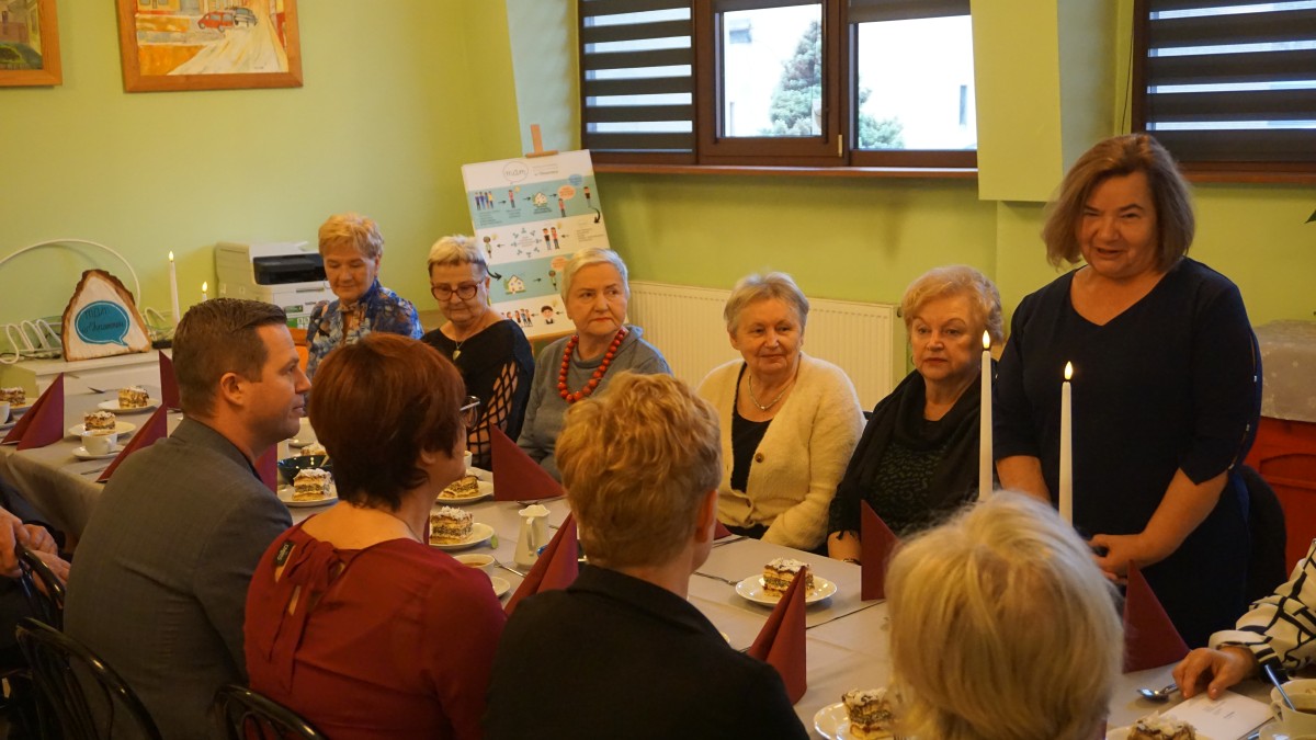 Zebrani siedzą przy wspólnym stole. Słuchają wypowiedzi Przewodniczącej Rady, która stoi.