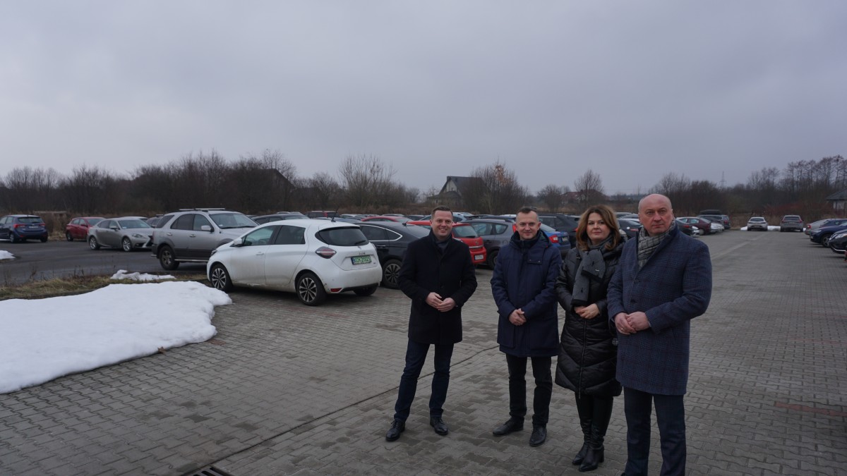 Cztery osoby stoją obok siebie. W tle widać parking i zaparkowane samochody.