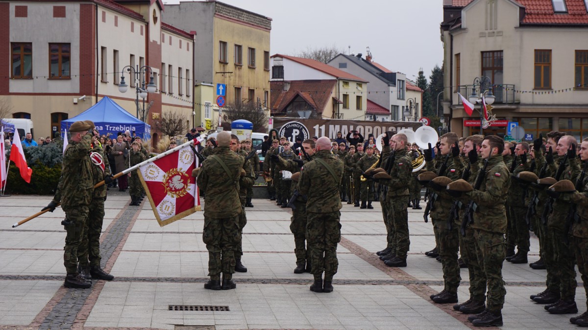 Zdjęcie, na pierwszym planie widać żołnierzy, którzy składają przysięgę na płycie rynku w Trzebini. W tle widac okierstrę i obseratorów. 